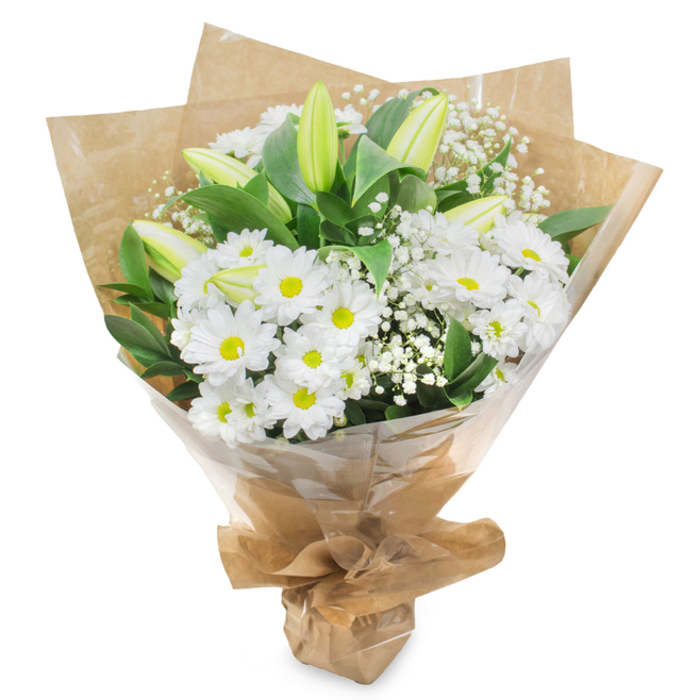 A serene white and green floral bouquet is photographed upright against a bright, uncluttered white background, allowing the subtle interplay of colour and texture to stand out clearly. At its core, clusters of daisy-like white chrysanthemums form a soft, rounded mass, each blossom with snowy petals and a distinct yellow-green center that adds warmth and gentle energy without disturbing the peaceful tone. Punctuating this cushion of daisies are several tall, unopened lily buds, their elongated shapes reaching slightly above the rest of the bouquet. These buds are pale green with hints of cream and soft white along the edges, their closed forms suggesting respect, contemplation, and the quiet unfolding of time. Threaded throughout are fine, branching stems of white gypsophila, whose countless tiny blooms create a delicate mist, filling gaps and giving the arrangement a light, airy feel, like morning fog over a calm space in Peckham Rye Park. Encircling the flowers is an assortment of lush green leaves, broad and gleaming, likely Ruscus or Salal, each leaf adding structure and a gentle frame that makes the white flowers appear even purer. The stems are gathered in a firm, tidy bundle and wrapped first in crinkled brown kraft paper that peeks above the flowers in soft, angular folds, lending a natural, rustic touch. Over this paper sits a clear veil of slightly crinkled cellophane, catching soft reflections and ensuring the bouquet is ready for careful delivery across Peckham, from Nunhead to Queens Road. The overall effect is graceful and composed, making this arrangement particularly suited to expressing sympathy, marking a loss with dignity, or sending a quiet message of healing and hope.